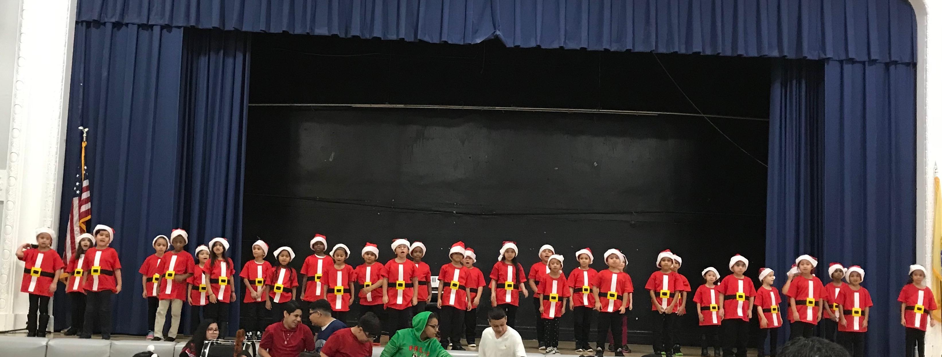 children on stage dressed as Santa's helpers signing